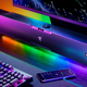 The Razer new Leviathan V2 Pro soundbar on a desk below a computer monitor with its RGB lighting creating a colored rainbow effect.